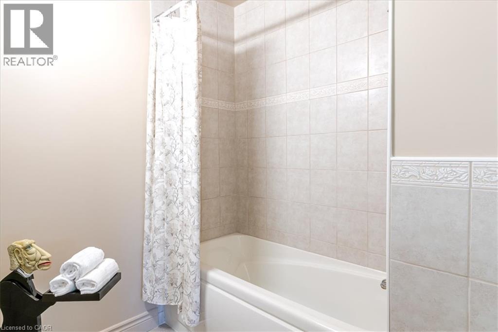 White bathtub with tile surround, featuring decorative accent tiles and a patterned shower curtain - 69 Pleasant Avenue, Hamilton, ON - Indoor Photo Showing Bathroom