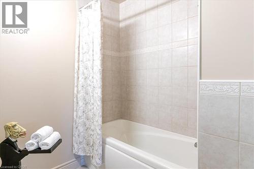 White bathtub with tile surround, featuring decorative accent tiles and a patterned shower curtain - 69 Pleasant Avenue, Hamilton, ON - Indoor Photo Showing Bathroom