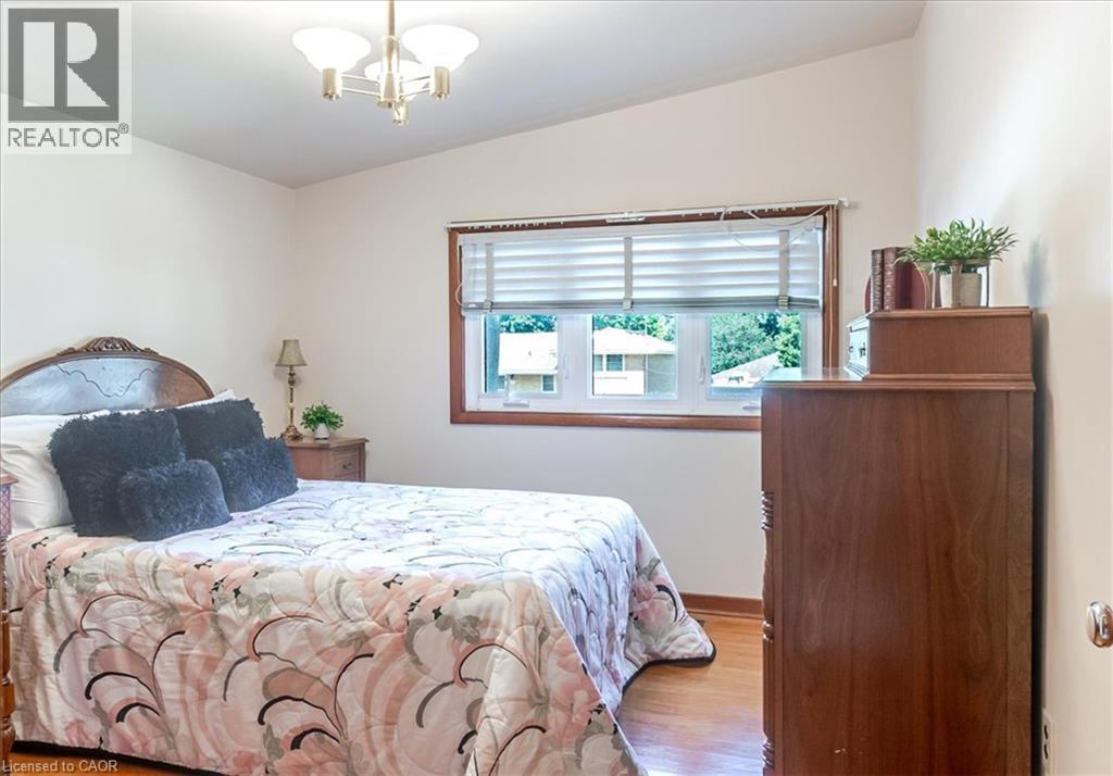 Bright room featuring a prominent window with horizontal blinds, wood-finish flooring, white walls, and a ceiling-mounted light fixture - 69 Pleasant Avenue, Hamilton, ON - Indoor Photo Showing Bedroom