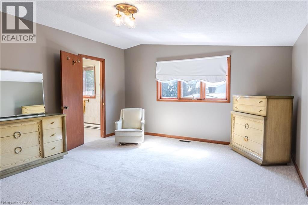 Neutral-toned bedroom featuring wall-to-wall carpeting, wood-trimmed windows with a roller shade, and a flush-mount ceiling light fixture - 69 Pleasant Avenue, Hamilton, ON - Indoor