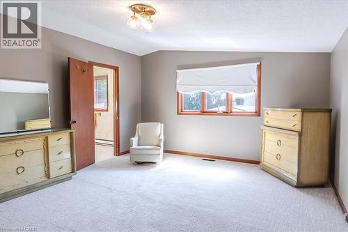 Neutral-toned bedroom featuring wall-to-wall carpeting, wood-trimmed windows with a roller shade, and a flush-mount ceiling light fixture - 69 Pleasant Avenue, Hamilton, ON - Indoor