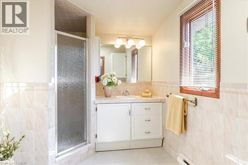 Bathroom featuring a white vanity with integrated sink, a large mirror with overhead lighting, a shower enclosure with a clear glass door, and a window with wood blinds - 69 Pleasant Avenue, Hamilton, ON - Indoor Photo Showing Bathroom