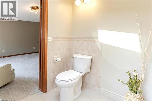 Renovated half bath featuring a two-piece toilet with elongated bowl, neutral tile wainscoting, brushed nickel wall sconce lighting, and decorative accent decor - 69 Pleasant Avenue, Hamilton, ON - Indoor Photo Showing Bathroom