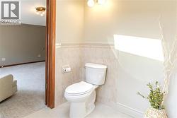 Renovated half bath featuring a two-piece toilet with elongated bowl, neutral tile wainscoting, brushed nickel wall sconce lighting, and decorative accent decor - 