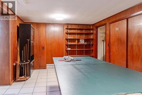 Spacious game room featuring rich wood-paneled walls, built-in shelving with display space, ceramic tile flooring, and recessed ceiling lighting - 69 Pleasant Avenue, Hamilton, ON - Indoor