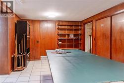Spacious game room featuring rich wood-paneled walls, built-in shelving with display space, ceramic tile flooring, and recessed ceiling lighting - 