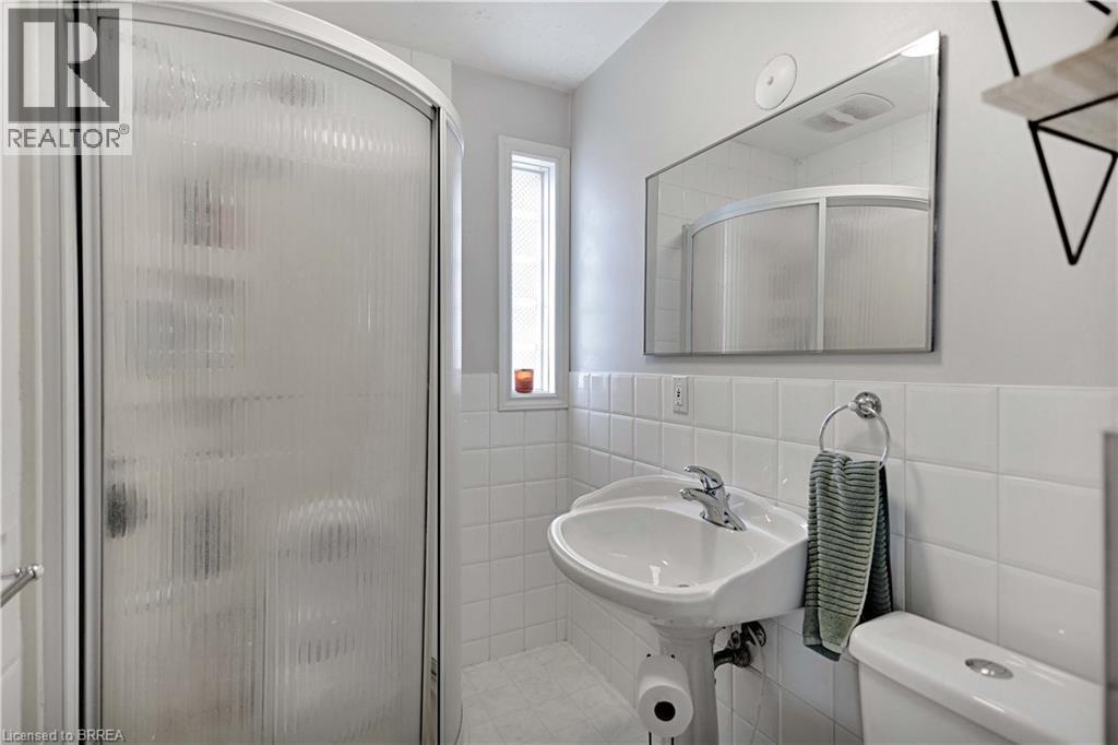 Compact bathroom featuring a curved shower enclosure with frosted glass, a pedestal sink with chrome faucet, a wall-mounted mirror, and white square tile wainscoting - 371 Ottawa Street S, Kitchener, ON - Indoor Photo Showing Bedroom