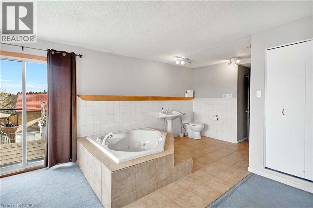 Built-in jetted tub surrounded by tile, pedestal sink, and toilet with tiled wall - 371 Ottawa Street S, Kitchener, ON - Indoor Photo Showing Bathroom