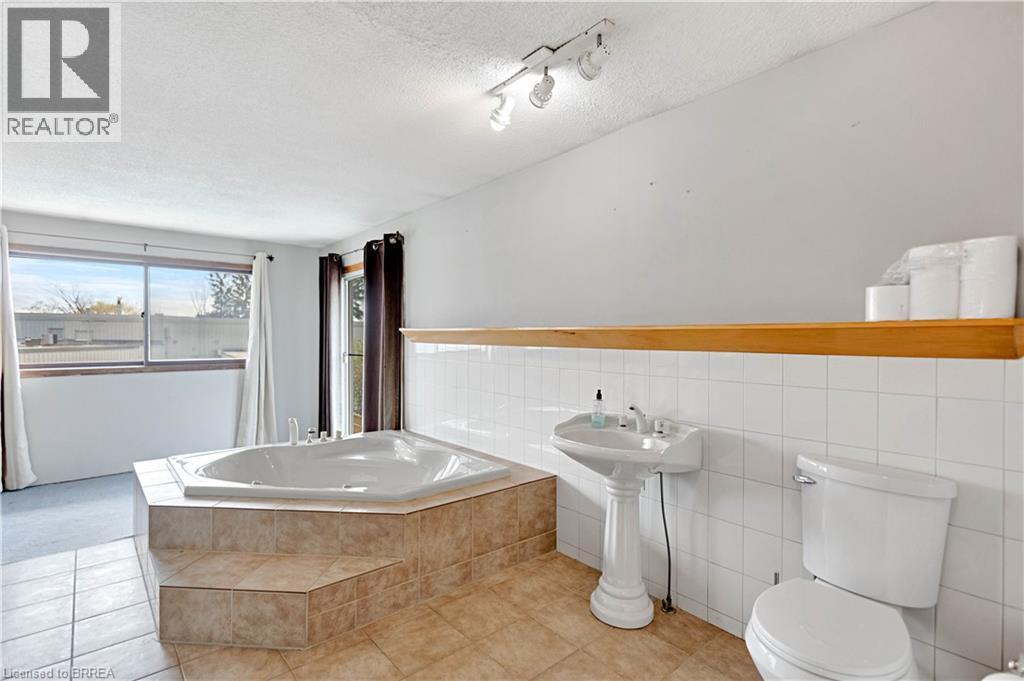 Spacious bathroom featuring an oversized corner soaking tub with tiled surround, pedestal sink, and tiled flooring - 371 Ottawa Street S, Kitchener, ON - Indoor Photo Showing Bedroom