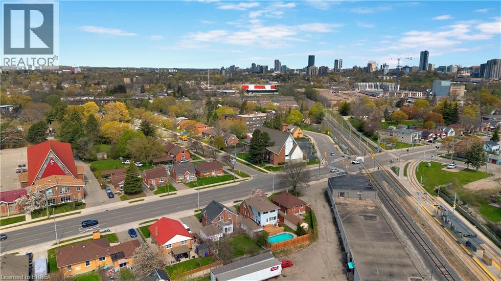Aerial perspective showcasing a mixed-use urban landscape with residential homes, mature trees, commercial buildings, and a distant city skyline - 371 Ottawa Street S, Kitchener, ON - Outdoor With View
