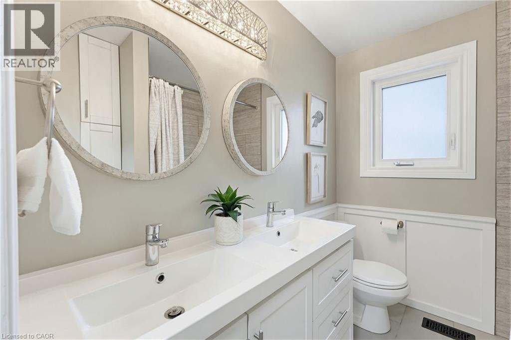 Contemporary bathroom featuring a double vanity with integrated sinks, two circular mirrors, and a modern light fixture - 60 Avenue Road, Cambridge, ON - Indoor Photo Showing Bathroom