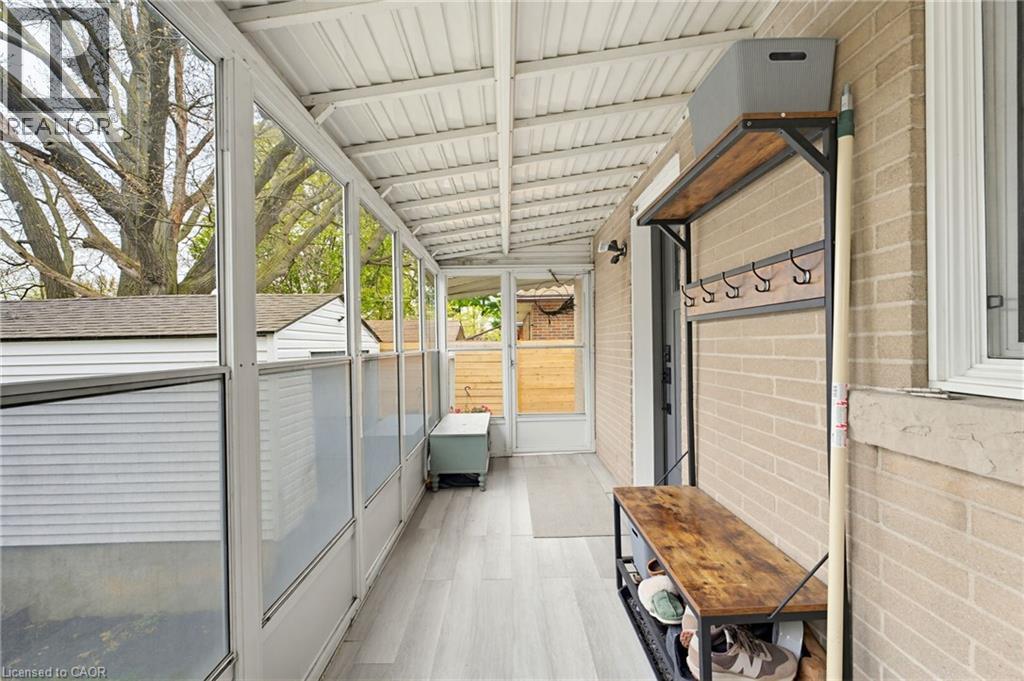Enclosed sunroom featuring light wood-finish flooring, a white corrugated ceiling, multiple large windows, and a brick exterior wall - 60 Avenue Road, Cambridge, ON - With Exterior