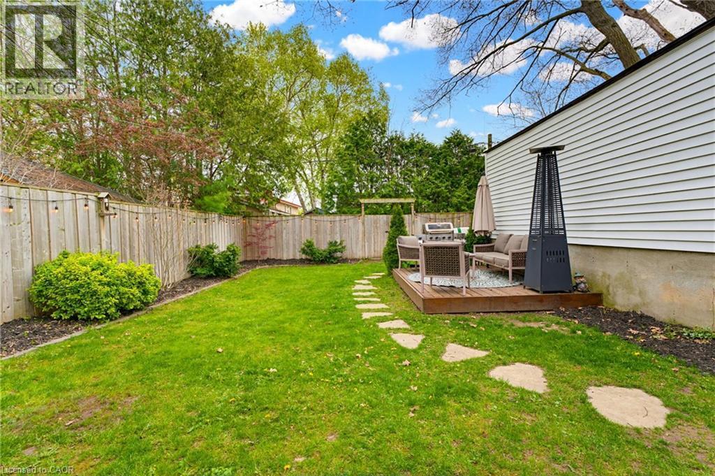 Private backyard featuring a wooden privacy fence with string lighting, mature landscaping, a stone paver pathway, and a wooden deck - 60 Avenue Road, Cambridge, ON - Outdoor