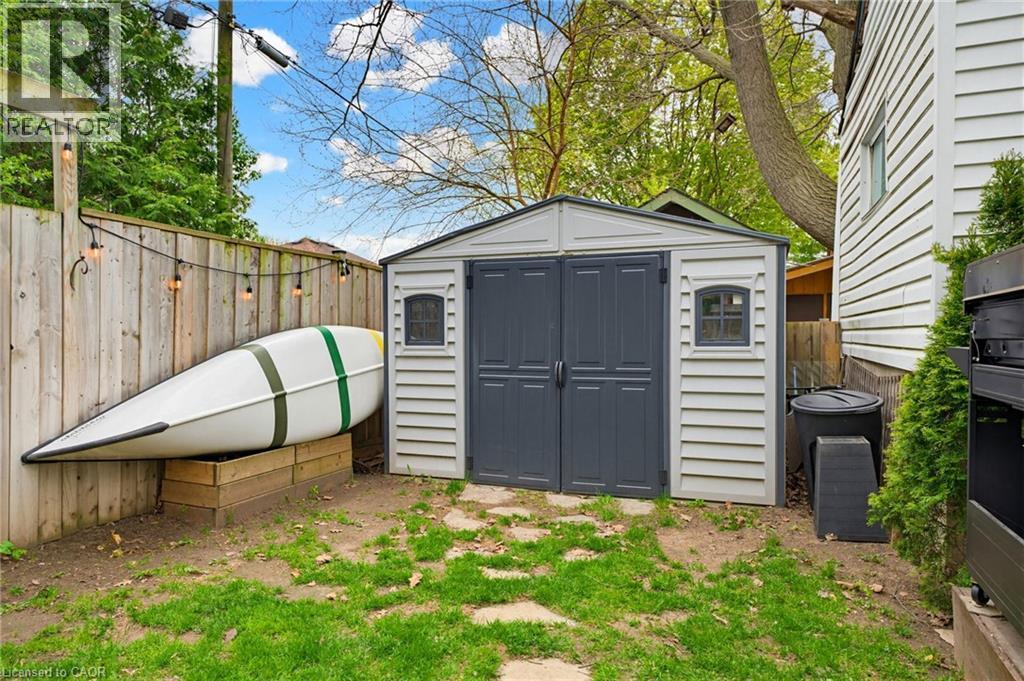 Compact backyard featuring a gray storage shed with double doors and window accents, perimeter wood fencing, and a stone paver path - 60 Avenue Road, Cambridge, ON - Outdoor