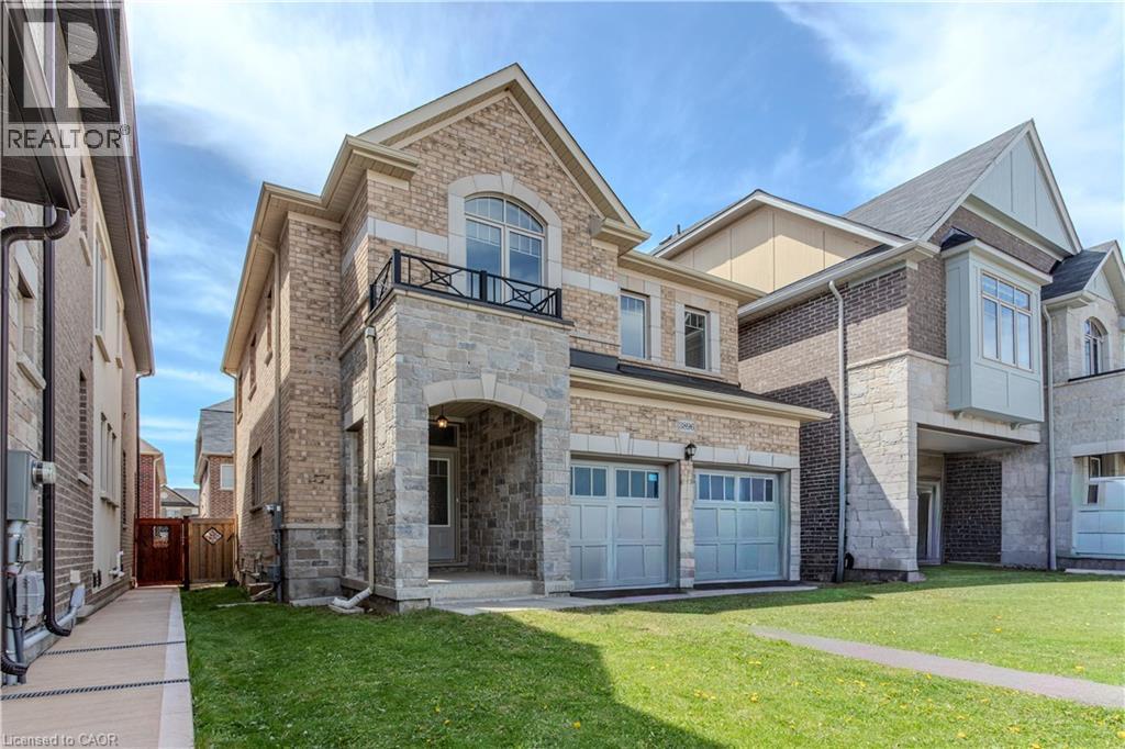 Two-story home featuring a stone and brick exterior, two garage bays with panel doors, an arched stone entryway, a second-story balcony with metal railing, and a side pathway leading to a wooden fence - 3896 Tufgar Crescent, Burlington, ON - Outdoor With Facade