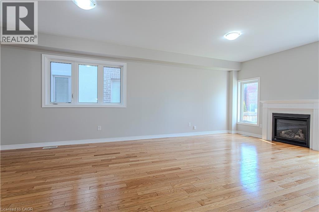 Spacious interior featuring wood-finish flooring, a contemporary fireplace with a white mantel, and multiple windows - 3896 Tufgar Crescent, Burlington, ON - Indoor Photo Showing Living Room With Fireplace