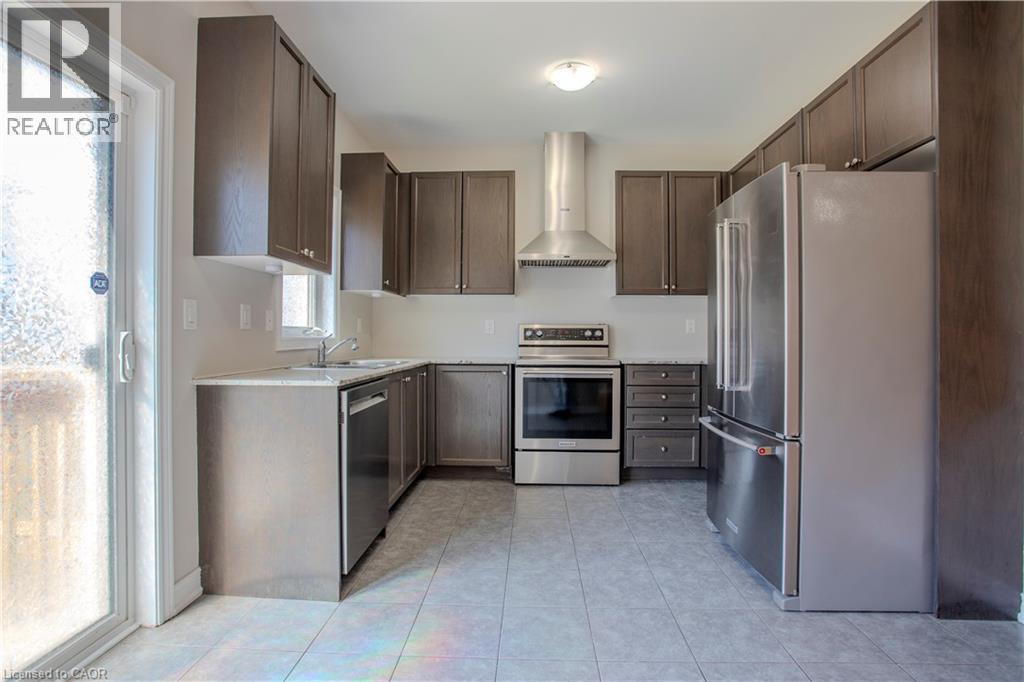 Modern kitchen featuring dark wood-finish cabinetry, stainless steel appliances, light-toned countertops, and a sliding glass door - 3896 Tufgar Crescent, Burlington, ON - Indoor Photo Showing Kitchen With Stainless Steel Kitchen