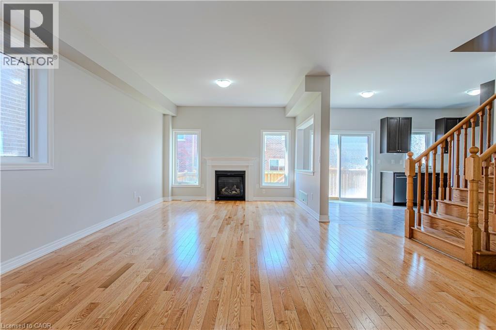 Expansive living area featuring light wood-finish flooring, a contemporary fireplace with a white mantel, multiple windows, recessed lighting, and a visible staircase with wood newel posts and baluste - 3896 Tufgar Crescent, Burlington, ON - Indoor Photo Showing Living Room With Fireplace