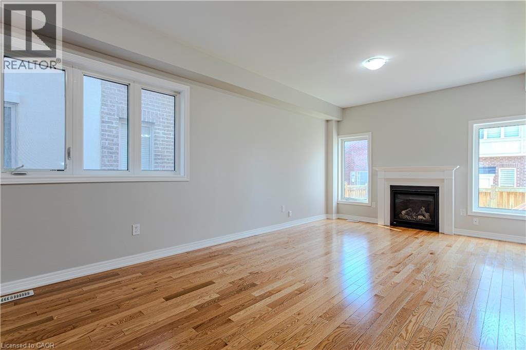 Spacious room featuring wood-finish flooring, a contemporary fireplace with a white mantel, multiple windows, and a ceiling-mounted light fixture - 3896 Tufgar Crescent, Burlington, ON - Indoor Photo Showing Living Room With Fireplace