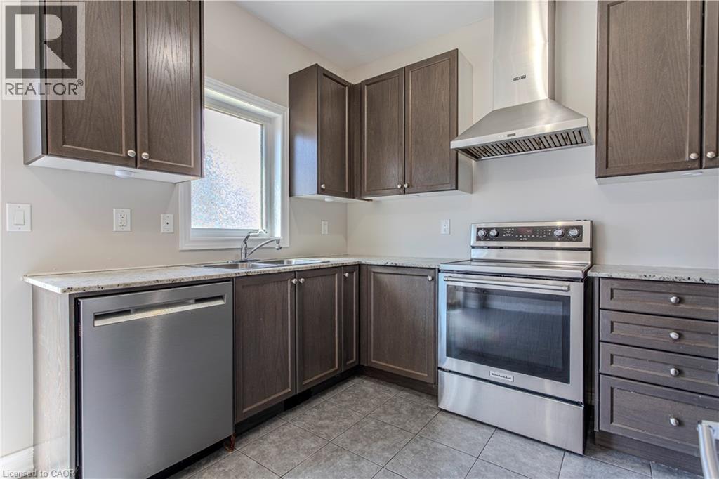 Contemporary kitchen featuring dark wood-finish cabinetry, light-toned countertops, a stainless steel dishwasher, a stainless steel range with a coordinating hood vent, and tile flooring - 3896 Tufgar Crescent, Burlington, ON - Indoor Photo Showing Kitchen With Stainless Steel Kitchen