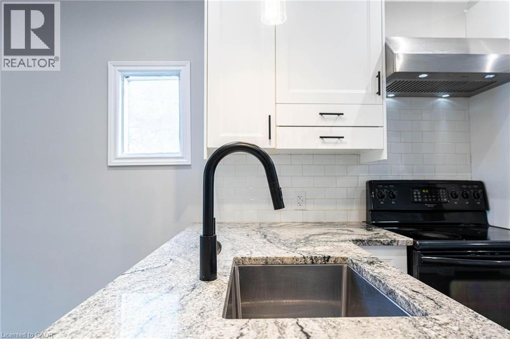Kitchen view of electric range, tasteful backsplash, white cabinetry, and light stone countertops - 222 Kensington Avenue N, Hamilton, ON - Indoor Photo Showing Kitchen