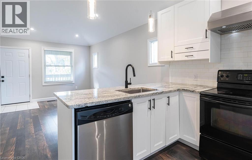 Kitchen featuring black / electric stove, tasteful backsplash, wall chimney range hood, dishwasher, and a peninsula - 222 Kensington Avenue N, Hamilton, ON - Indoor Photo Showing Kitchen