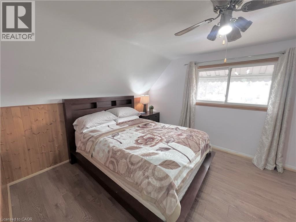 Bedroom featuring wood-finish flooring, a decorative wood accent wall, a white ceiling with a ceiling fan light fixture, and a window with a wood-trimmed frame - 56 Eastvale Place, Hamilton, ON - Indoor Photo Showing Bedroom