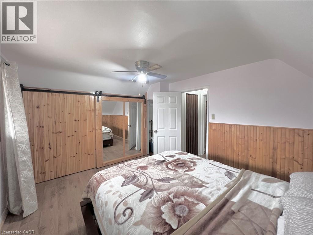 Interior space featuring wood-finish flooring, a wood-paneled accent wall, and a ceiling fan with integrated lighting - 56 Eastvale Place, Hamilton, ON - Indoor Photo Showing Bedroom