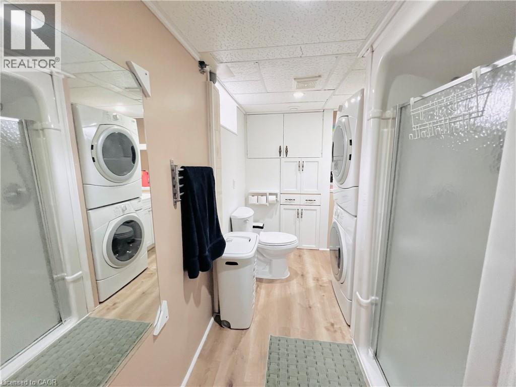 Full bathroom featuring a shower stall with clear glass, wood-finish flooring, and a white toilet - 56 Eastvale Place, Hamilton, ON - Indoor Photo Showing Laundry Room