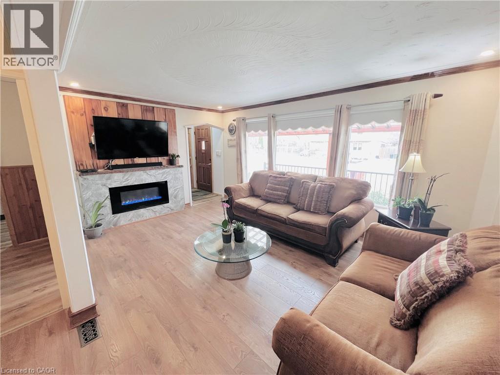 Living room featuring light wood-finish flooring, an electric fireplace with a stone surround, and wood paneling - 56 Eastvale Place, Hamilton, ON - Indoor Photo Showing Living Room With Fireplace