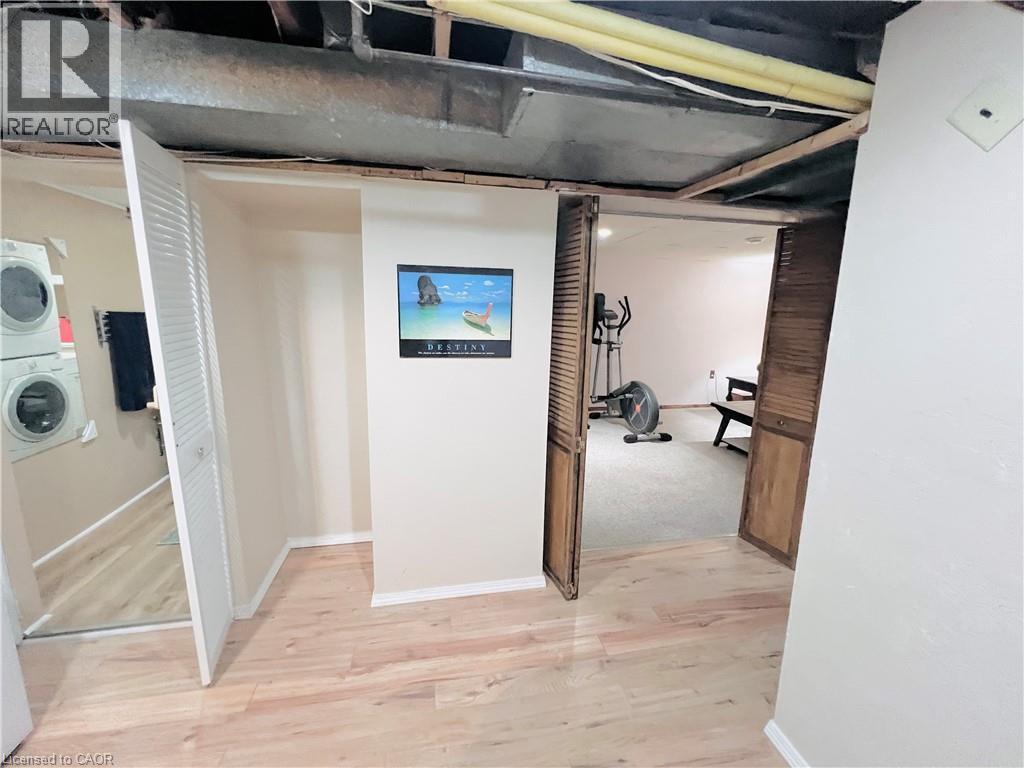 Hardwood-style flooring extends into a laundry area with stacked appliances, complemented by louvered closet doors and exposed ceiling joists - 56 Eastvale Place, Hamilton, ON -