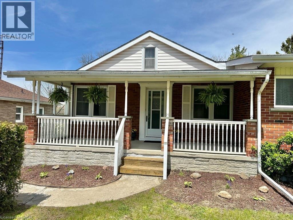 Brick exterior featuring a covered porch with white railing, white columns, and a front entry door with sidelights - 165 Highway 6, Simcoe, ON - Outdoor With Deck Patio Veranda