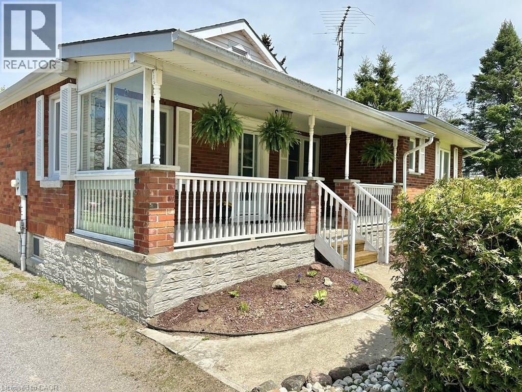 Brick exterior featuring a covered porch with white railings, a three-step entry, and decorative columns - 165 Highway 6, Simcoe, ON - Outdoor