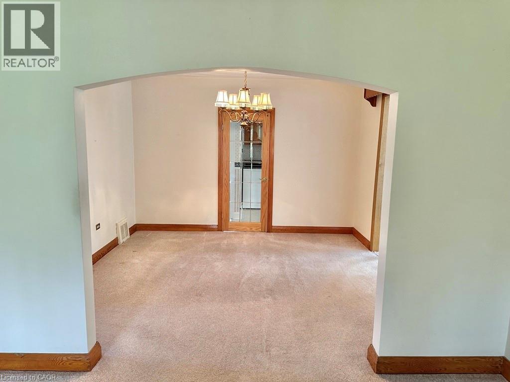 Archway entry to a carpeted room featuring a chandelier and a glass-paneled door with wood trim - 165 Highway 6, Simcoe, ON - Indoor Photo Showing Other Room