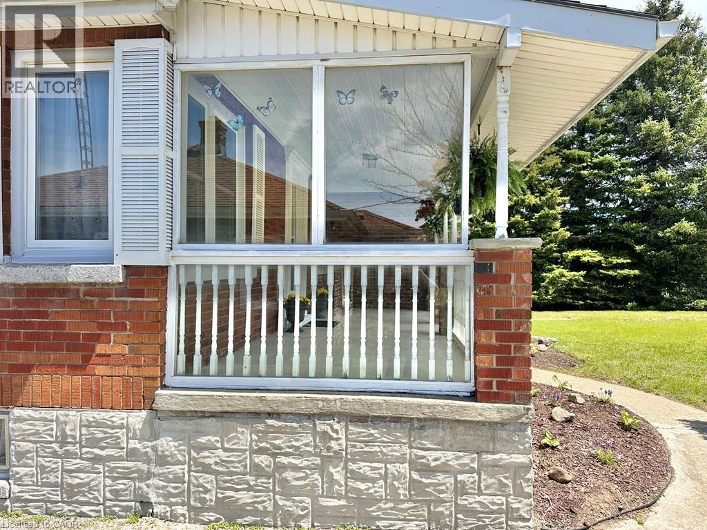 Brick and stone facade featuring a screened-in porch with white railing, covered entry, and white window shutters - 165 Highway 6, Simcoe, ON - Outdoor