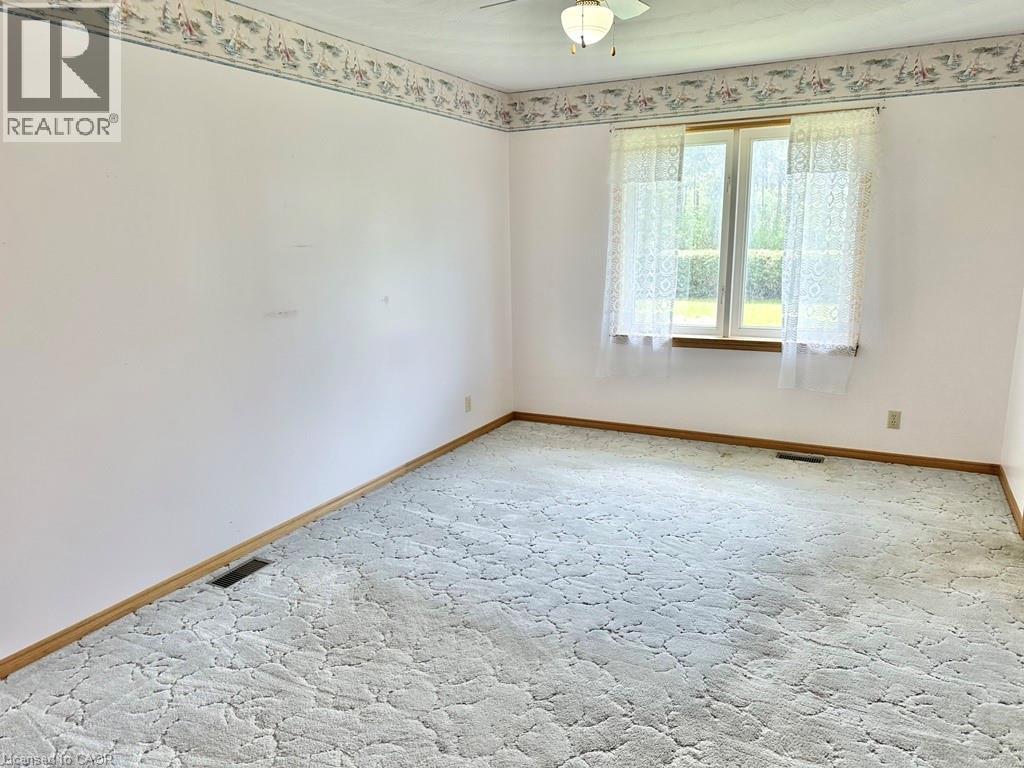 Light-filled interior space featuring a double window with wood trim, wall-to-wall patterned carpeting, white painted walls, and a ceiling fan with integrated lighting - 165 Highway 6, Simcoe, ON - Indoor Photo Showing Other Room