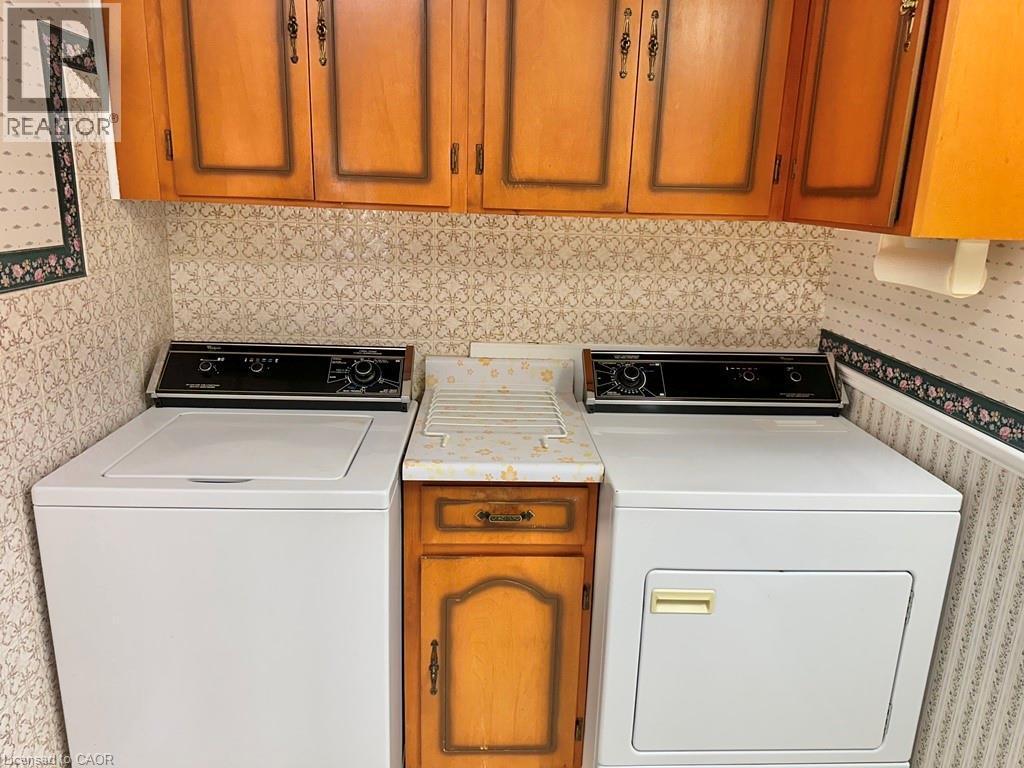 Laundry area featuring wood-finish cabinetry, a built-in folding rack, and patterned wallpaper - 165 Highway 6, Simcoe, ON - Indoor Photo Showing Laundry Room
