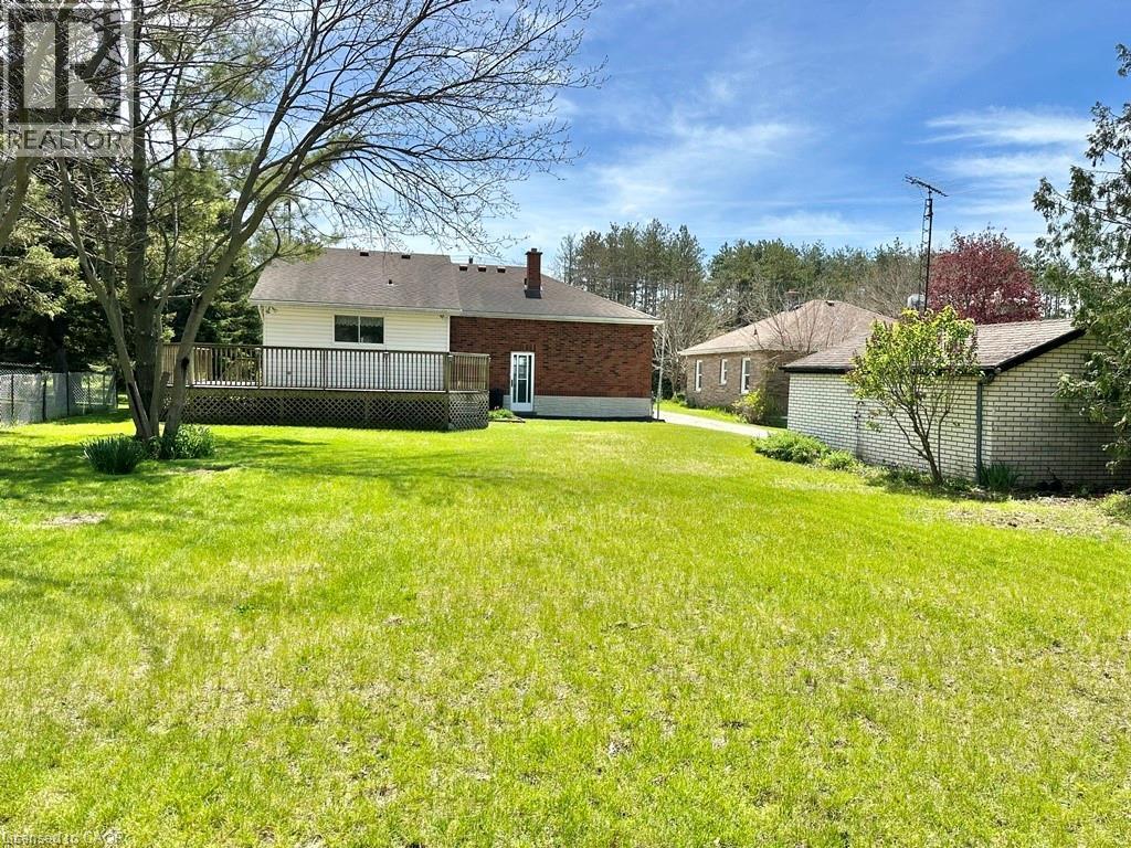 Expansive rear yard featuring green lawn space, a substantial wood deck, and mature trees - 165 Highway 6, Simcoe, ON - Outdoor