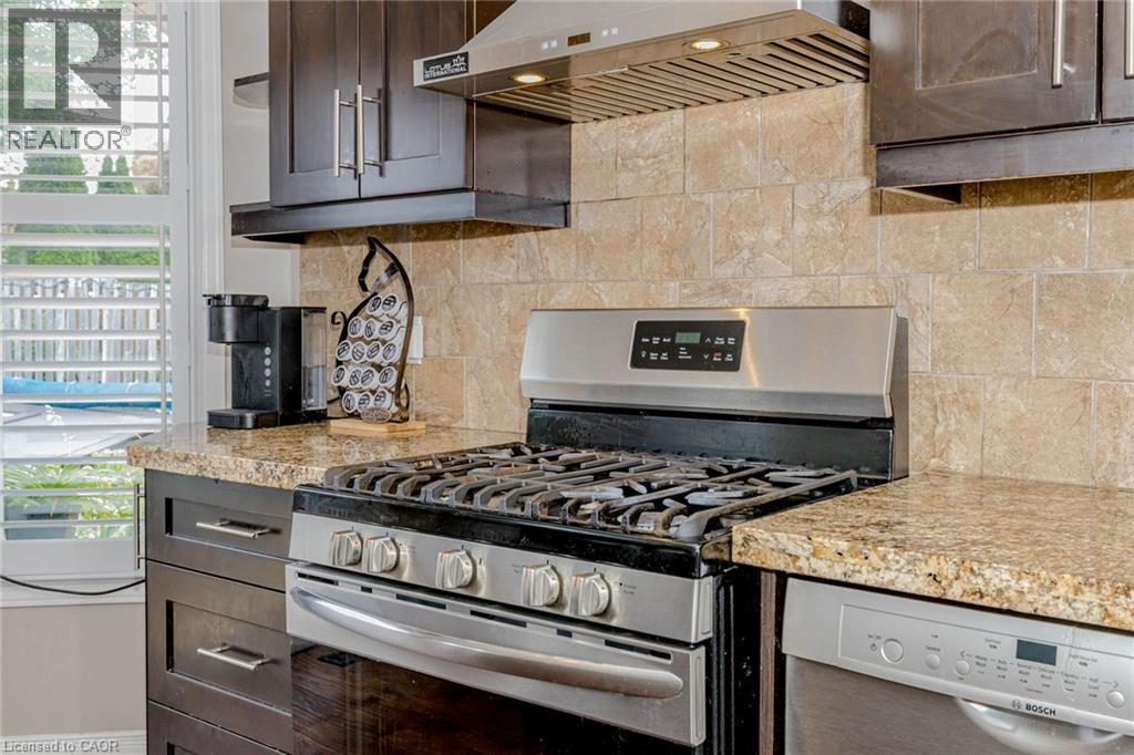 Kitchen with stainless steel appliances, dark wood finish cabinets, backsplash, and light stone countertops - 32 Vineberg Drive, Hamilton, ON - Indoor Photo Showing Kitchen