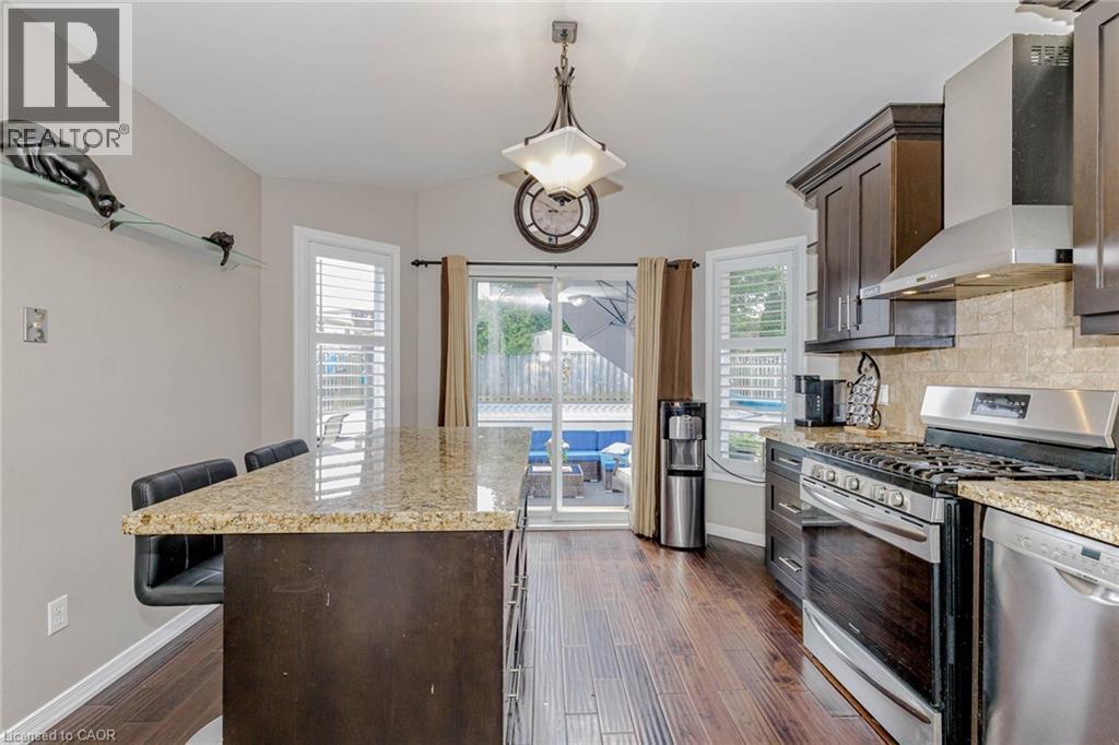 Kitchen with dark wood finish cabinetry, stainless steel appliances, a breakfast bar, light stone countertops, and a kitchen island - 32 Vineberg Drive, Hamilton, ON - Indoor Photo Showing Kitchen With Upgraded Kitchen