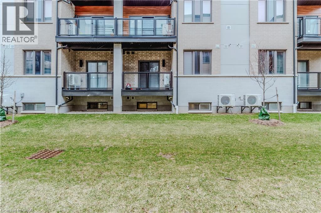 Back of property with brick siding, ac unit, and a yard - 25 Isherwood Avenue Unit# G-105, Cambridge, ON - Outdoor With Facade