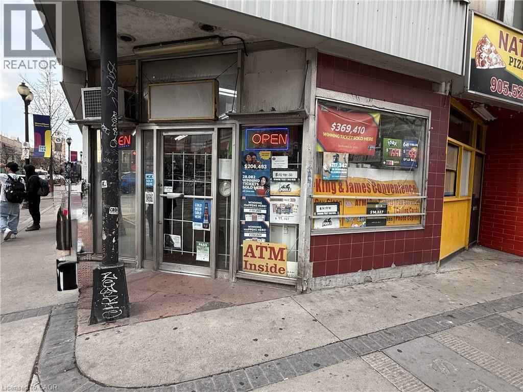 Corner commercial storefront featuring prominent window displays, a red tiled facade, and a glass entrance door - 1 King Street E, Hamilton, ON
