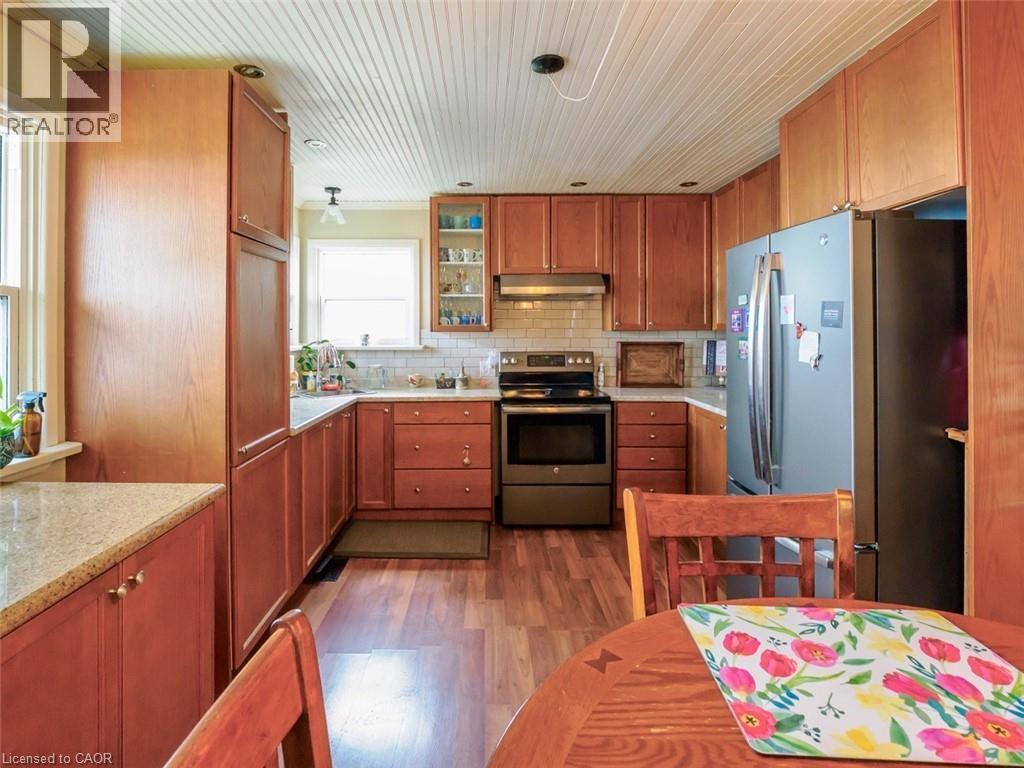 Kitchen featuring wood cabinetry, light countertops, subway tile backsplash, stainless steel appliances, and wood-finish flooring - 1395 Lakeshore Road, Haldimand County, ON - Indoor Photo Showing Dining Room