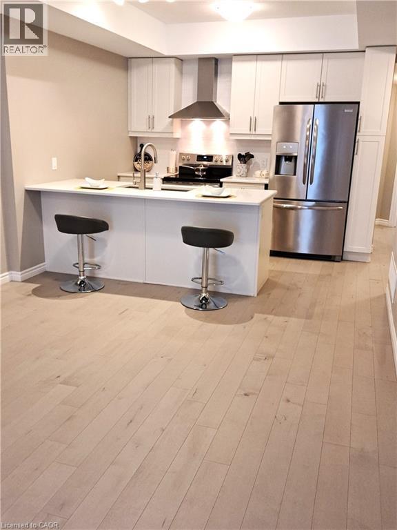 Kitchen featuring light wood-finish flooring, white cabinetry, stainless steel appliances, and a central island with countertop seating - 26 Wheat Lane, Kitchener, ON - Indoor Photo Showing Kitchen