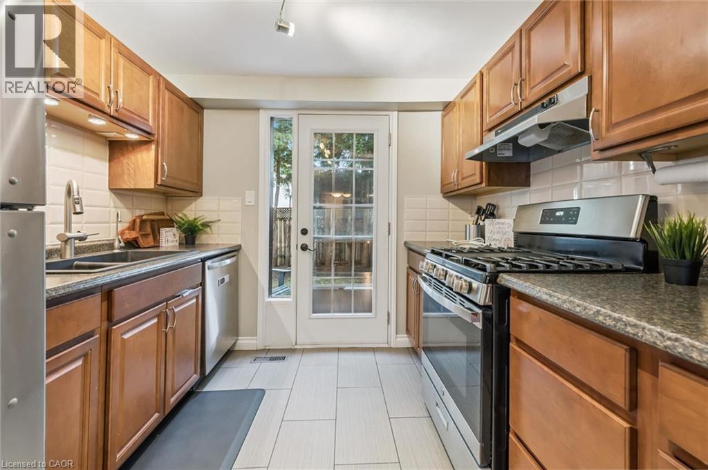 Galley kitchen featuring wood cabinetry, stainless steel appliances, light tile flooring, dark countertops, and a full-light door - 460 Parkview Crescent, Cambridge, ON - Indoor Photo Showing Kitchen With Double Sink