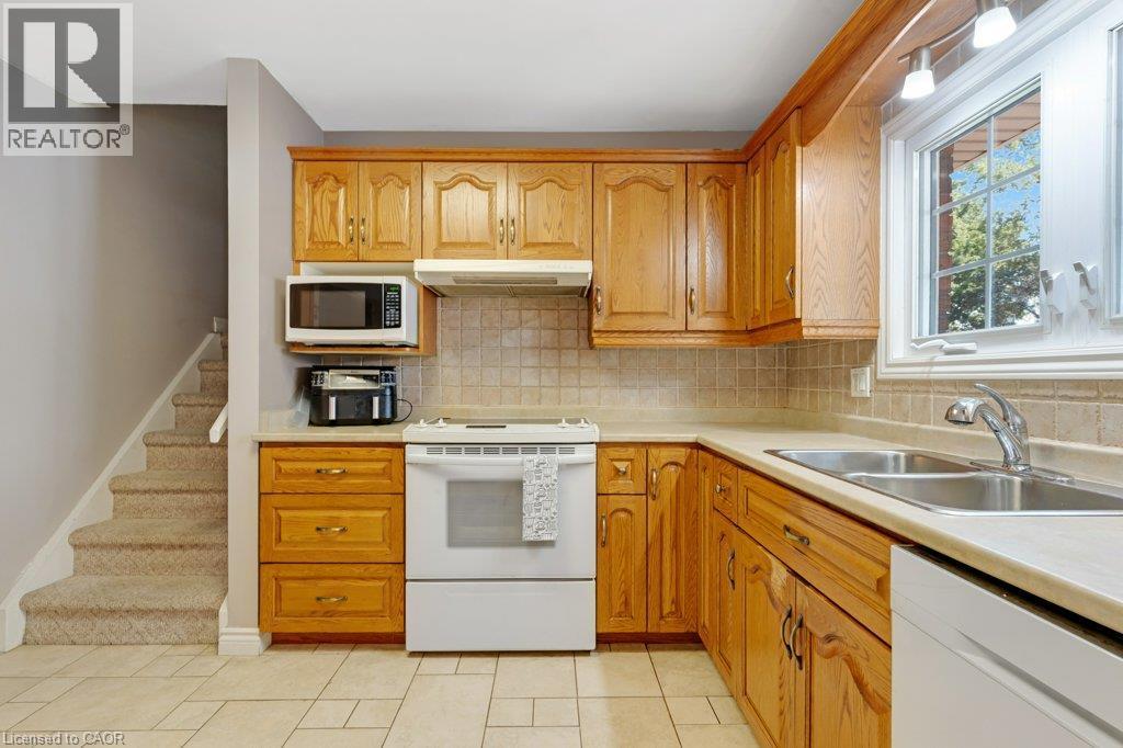 Kitchen featuring wood-finish cabinetry, tile backsplash, laminate countertops, and a double basin stainless steel sink - 236 Winston Boulevard, Cambridge, ON - Indoor Photo Showing Kitchen With Double Sink