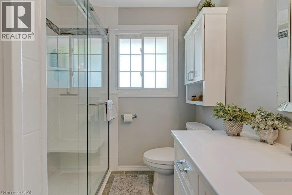 Glass-enclosed shower with a built-in bench, white vanity with an integrated sink, white upper cabinetry, and a grid-patterned window - 236 Winston Boulevard, Cambridge, ON - Indoor Photo Showing Bathroom