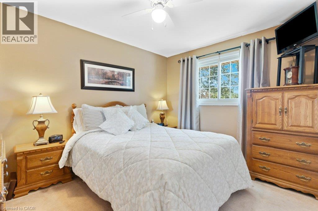 Neutral tone wall paint, flush mount ceiling fan, window with exterior foliage, carpeted flooring, and a decorative picture frame - 236 Winston Boulevard, Cambridge, ON - Indoor Photo Showing Bedroom