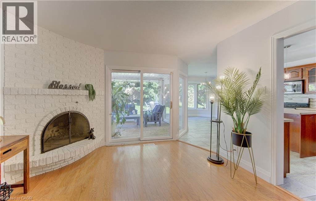 Living area featuring a white-painted brick fireplace with a metal fire screen, wood-finish flooring, and sliding glass doors opening to an outdoor patio - 106 Autumn Hill Crescent, Kitchener, ON - Indoor With Fireplace