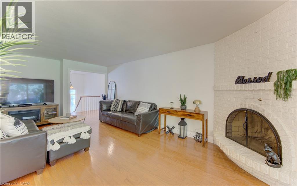 Living area featuring a painted brick corner fireplace with an arched firebox, light wood-finish flooring, and white walls - 106 Autumn Hill Crescent, Kitchener, ON - Indoor Photo Showing Living Room With Fireplace